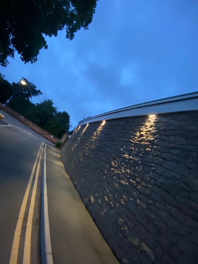 Curved stone boundary wall with warm downlighting at dusk